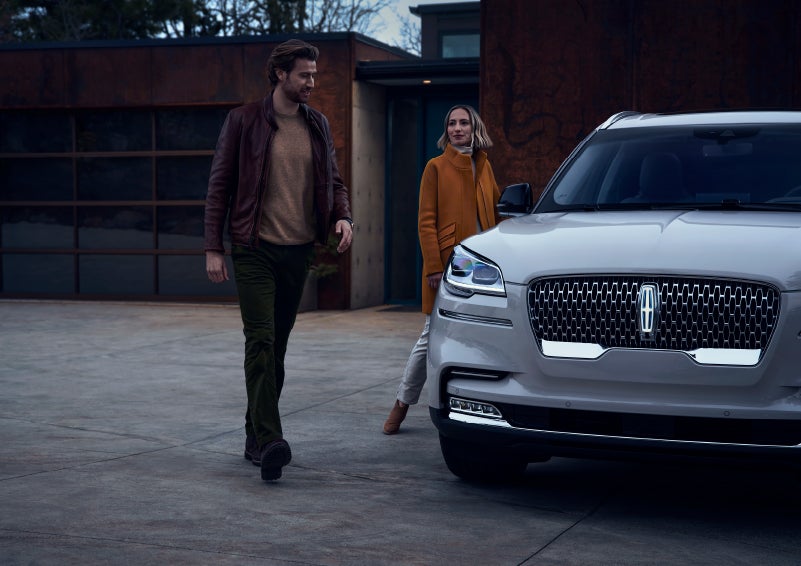 A man and a woman approaching a 2024 Lincoln Aviator® SUV, which illuminates certain lights when they are close | Sedano Lincoln in La Mesa CA
