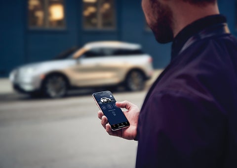 A person is shown interacting with a smartphone to connect to a Lincoln vehicle across the street. | Sedano Lincoln in La Mesa CA