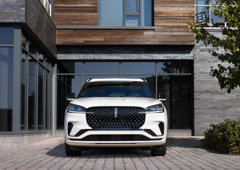A white 2025 Lincoln Aviator® SUV is shown parked outside a modern building with gray brick and wood accents. | Sedano Lincoln in La Mesa CA