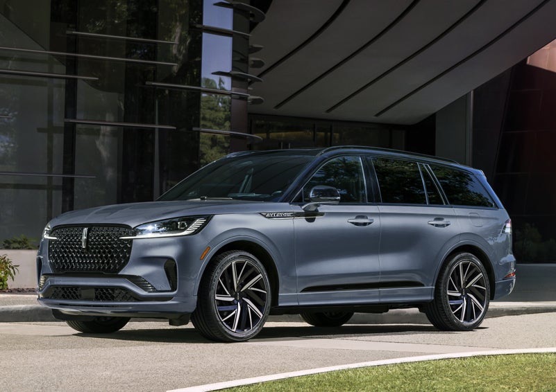 A gray 2025 Lincoln Aviator® SUV is parked outside a modern building showcasing the driver’s side of the vehicle. | Sedano Lincoln in La Mesa CA