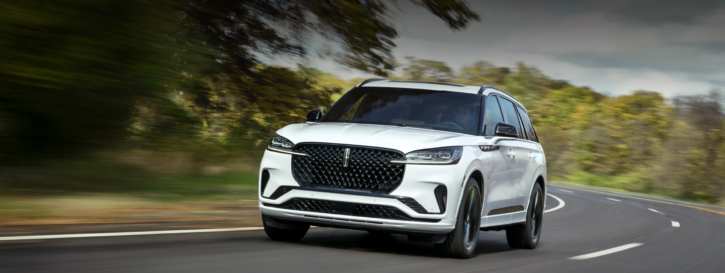 A white 2025 Lincoln Aviator® SUV is being driven down a road lined with trees. | Sedano Lincoln in La Mesa CA