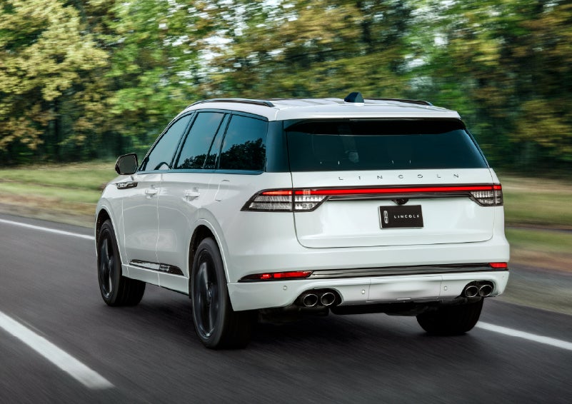 A white 2026 Lincoln Aviator® SUV is being driven away down a road lined with colorful trees. | Sedano Lincoln in La Mesa CA