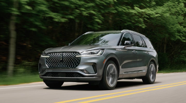 A 2027 Lincoln Aviator® SUV is being driven down a road lined with trees. | Sedano Lincoln in La Mesa CA